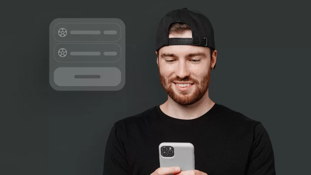 Homem de boné virado para trás olhando o celular, sobre fundo cinza neutro.